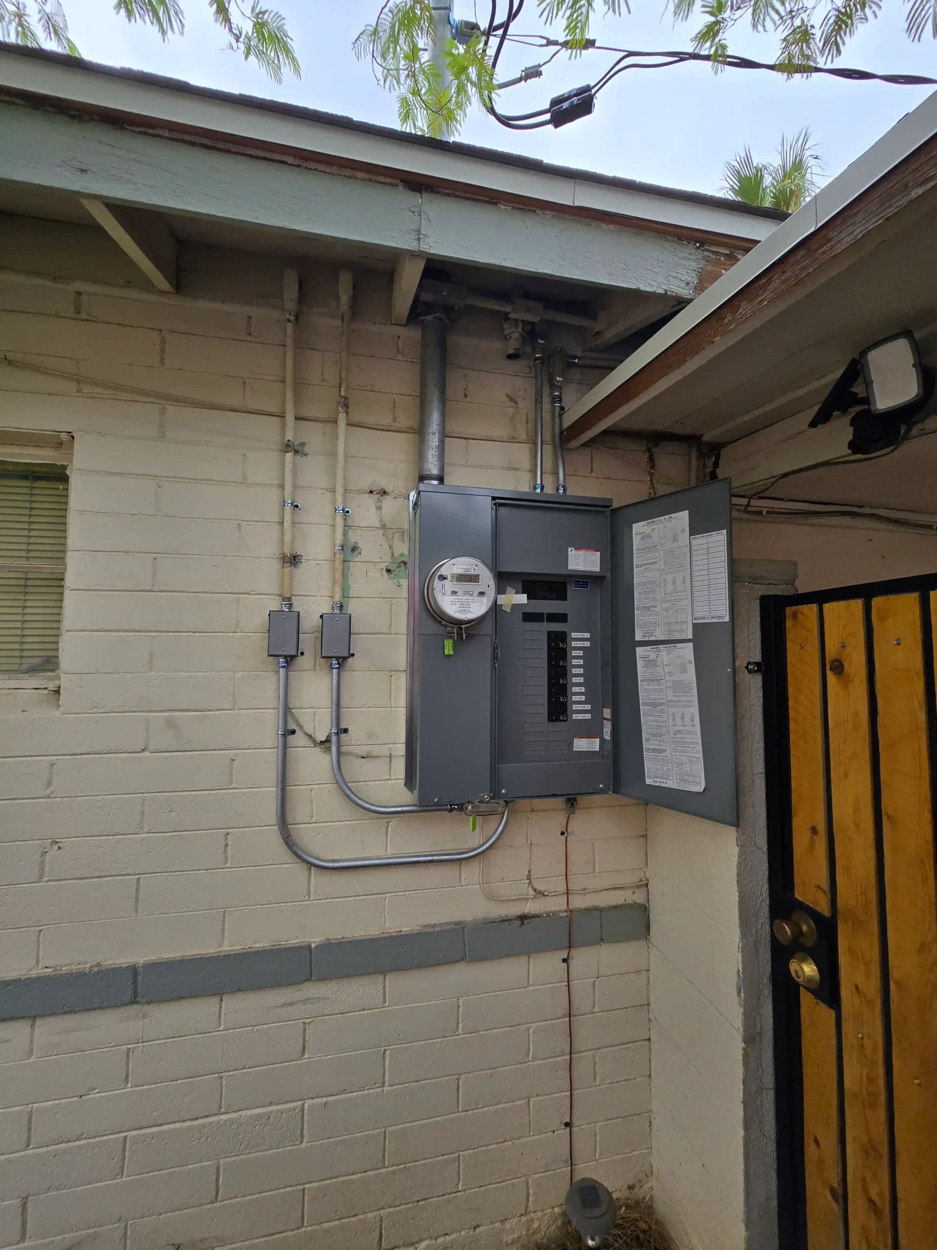 Electric meter and circuit breaker panel mounted on a residential wall with outdoor access.