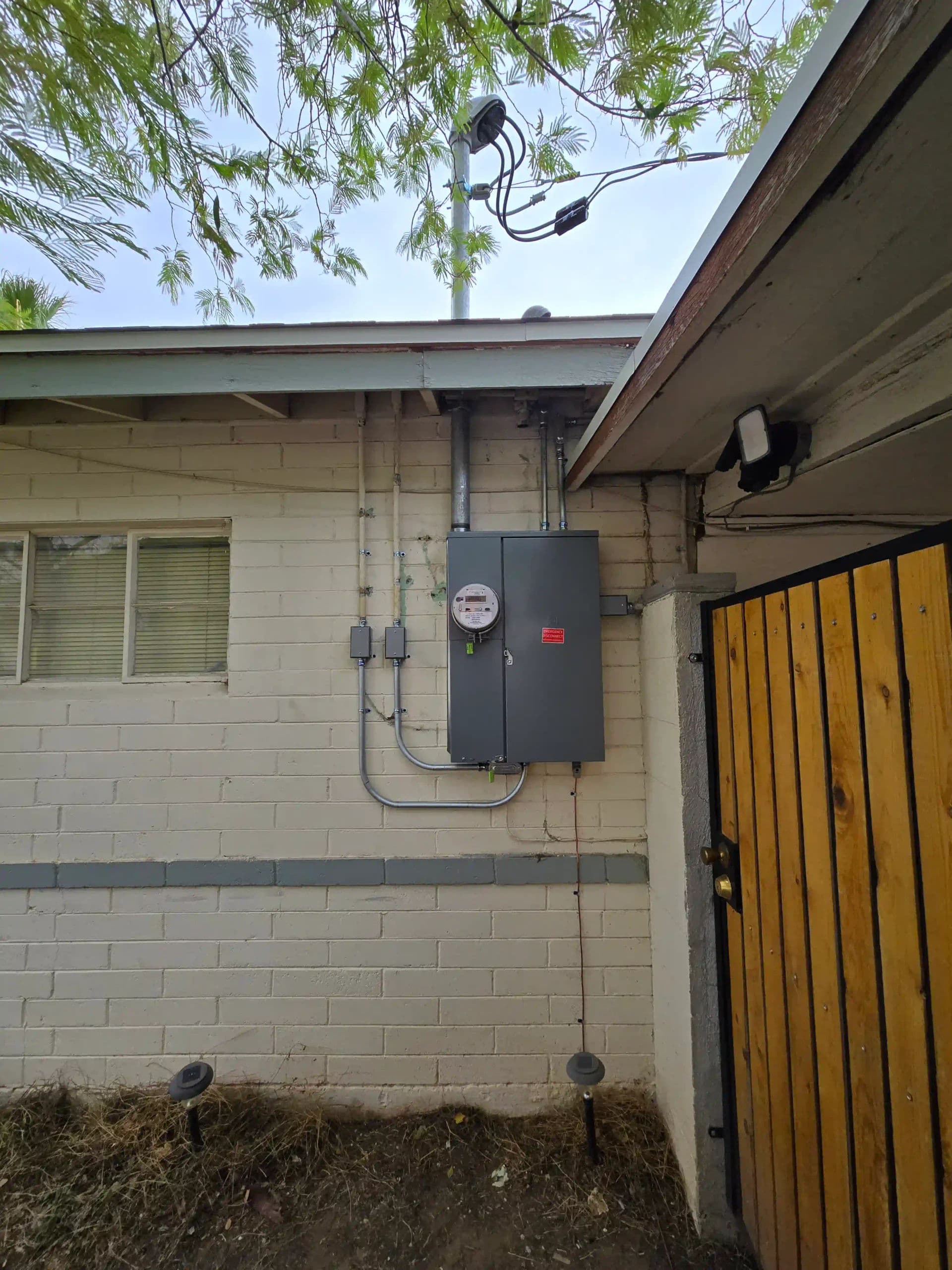 Electric meter and utility box mounted on a residential wall with outdoor features.