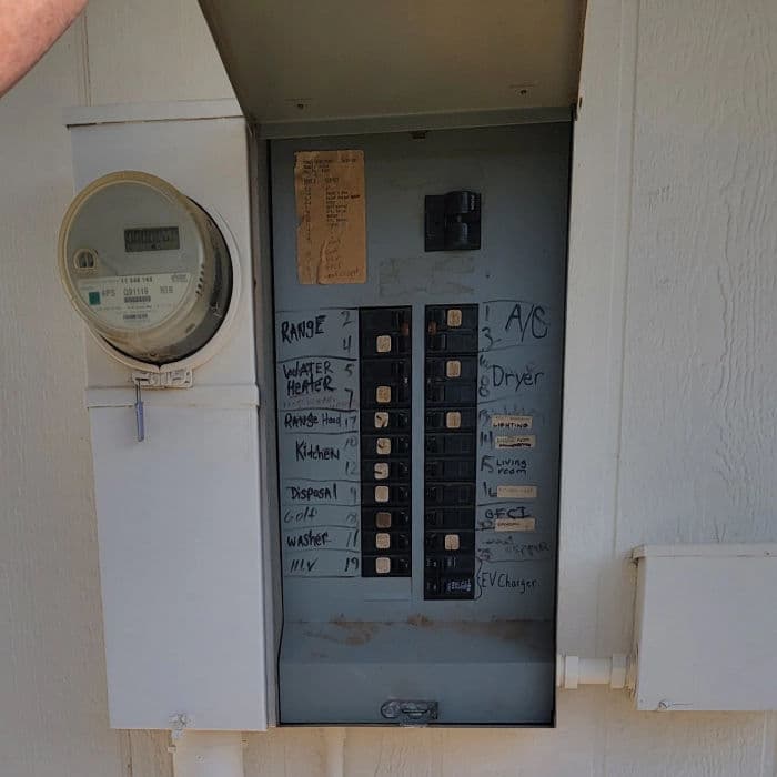 Electrical panel with labeled circuit breakers and a utility meter, located on a wall.