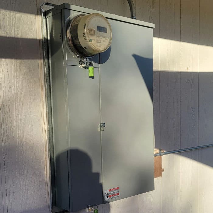 Electric meter mounted on a gray utility box against a textured wall.