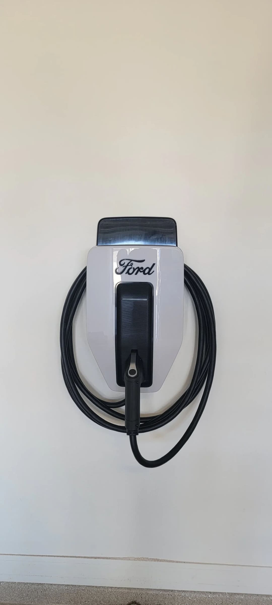 Ford electric vehicle charger mounted on a wall, featuring a sleek design and black charging cable.