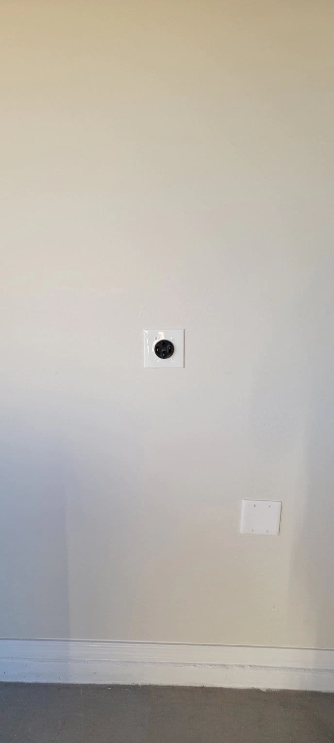 Wall outlet with black socket and white plate on a light-colored wall.