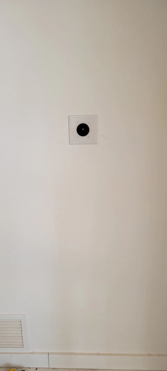Wall plate with a single round electrical outlet on a smooth white surface.