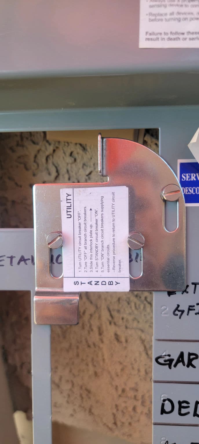 Metal utility bracket with safety instructions attached to a service panel.