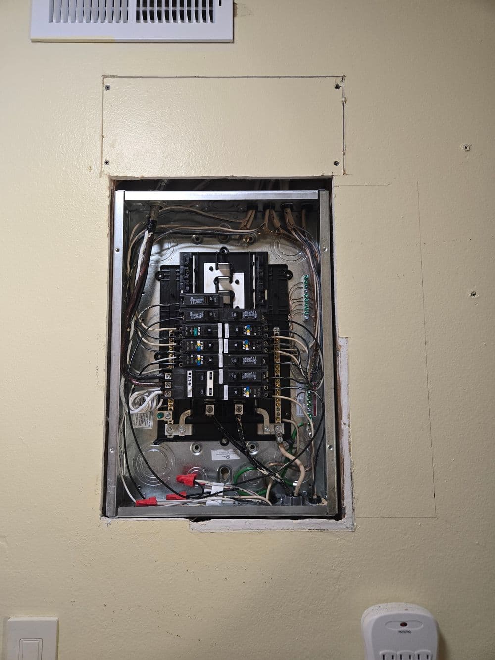 Electrical panel with circuit breakers and wiring on a beige wall.
