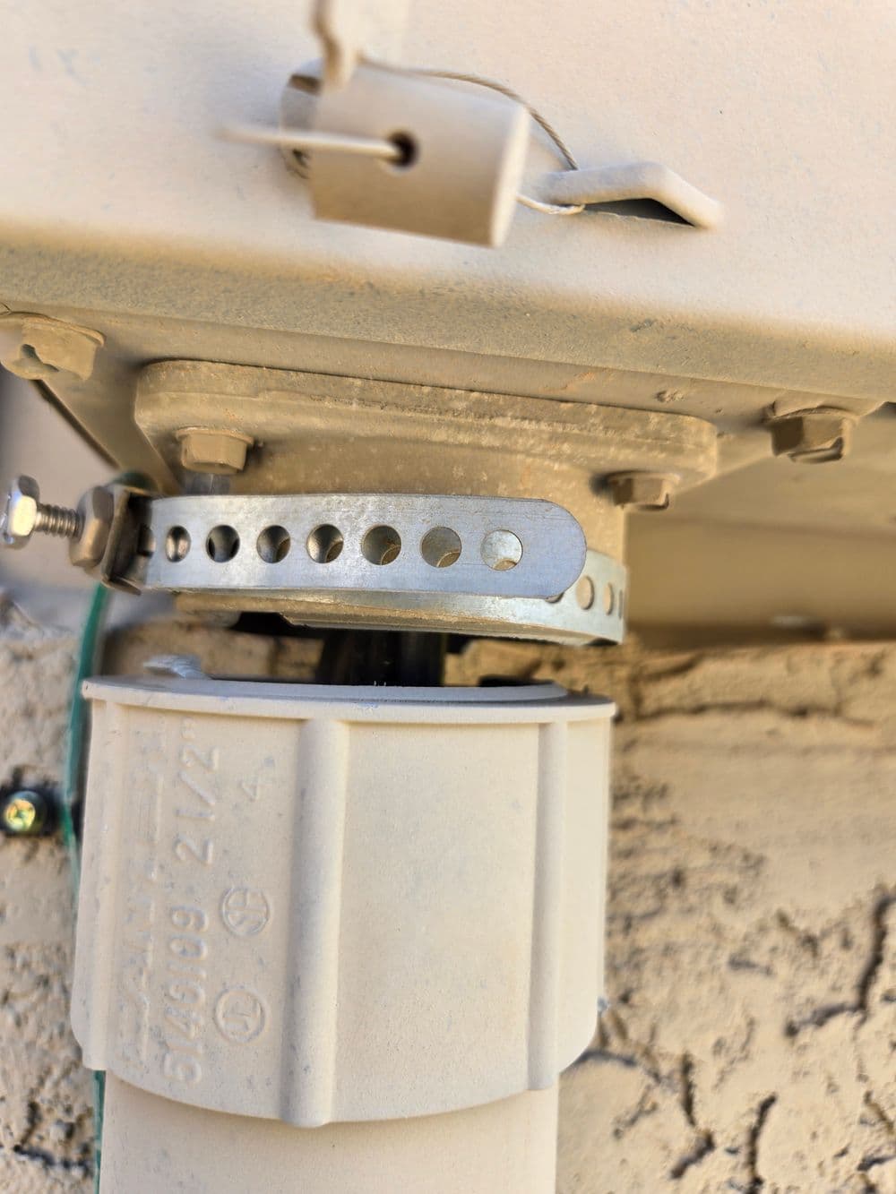 Close-up of a pipe connection with a metal clamp mounted on a textured wall.
