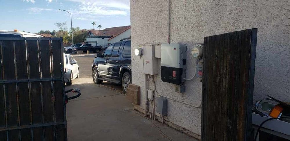 Utility meters and electrical box alongside a concrete driveway between two buildings.