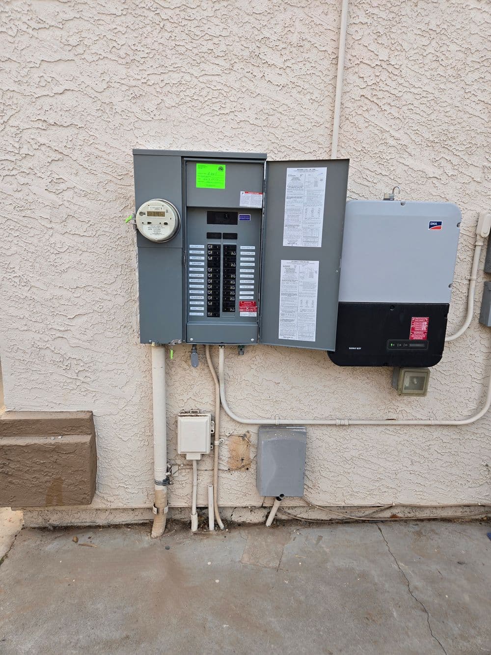 Electrical panel and smart meter installed on a beige wall, with visible circuit labels.