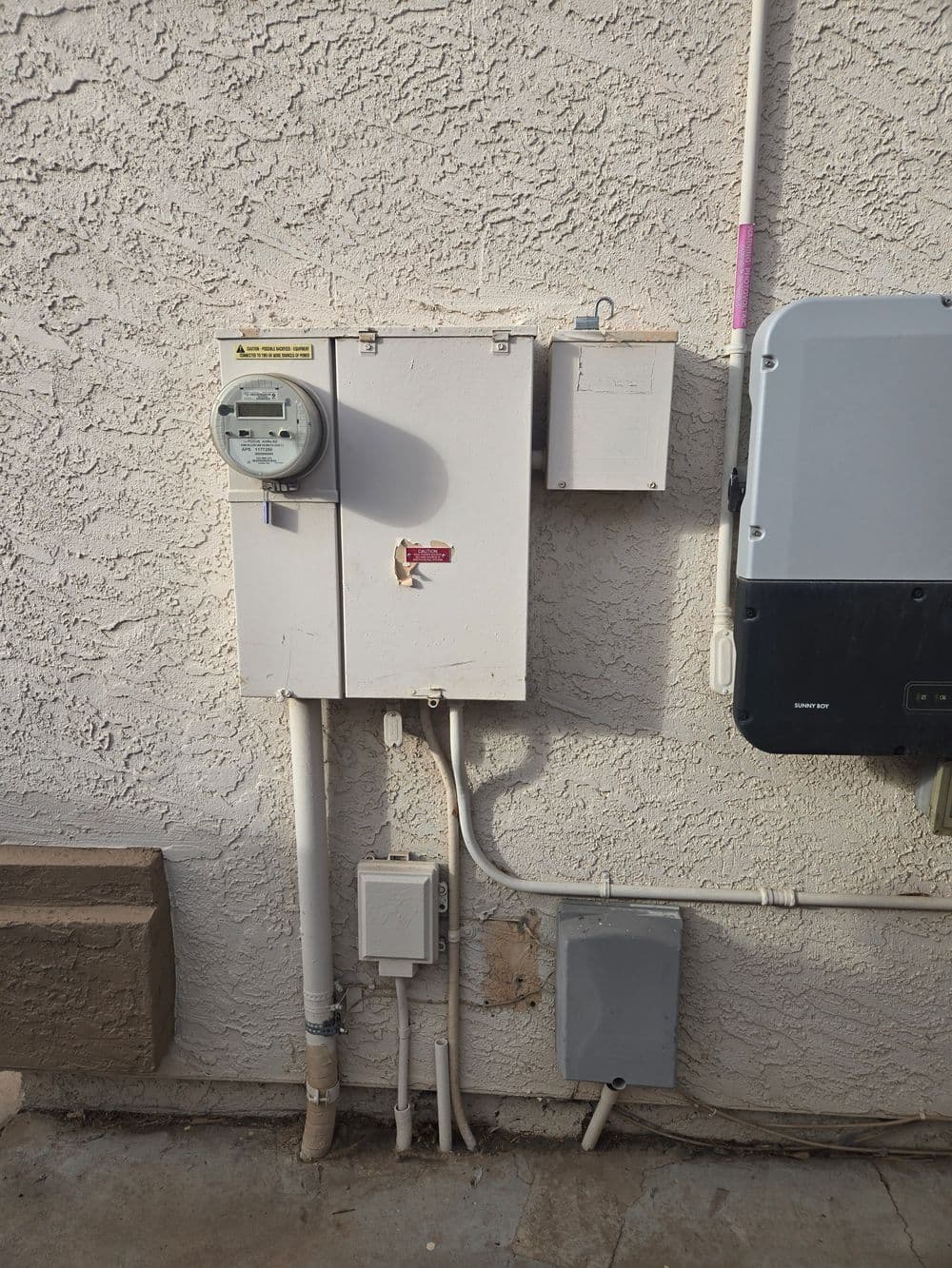 Electrical meter and panel mounted on textured wall, showing utility connections and equipment.