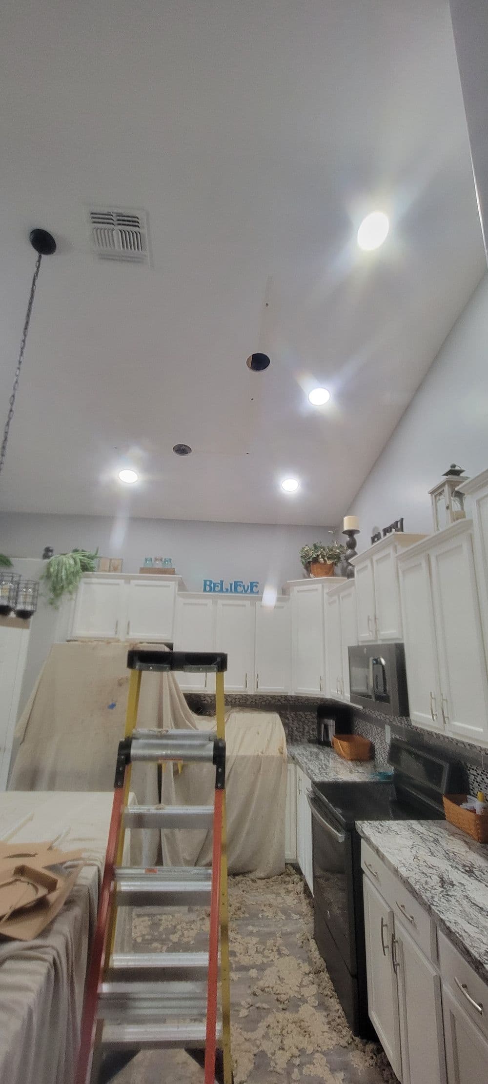 Modern kitchen under renovation with a ladder, recessed lighting, and covered surfaces.