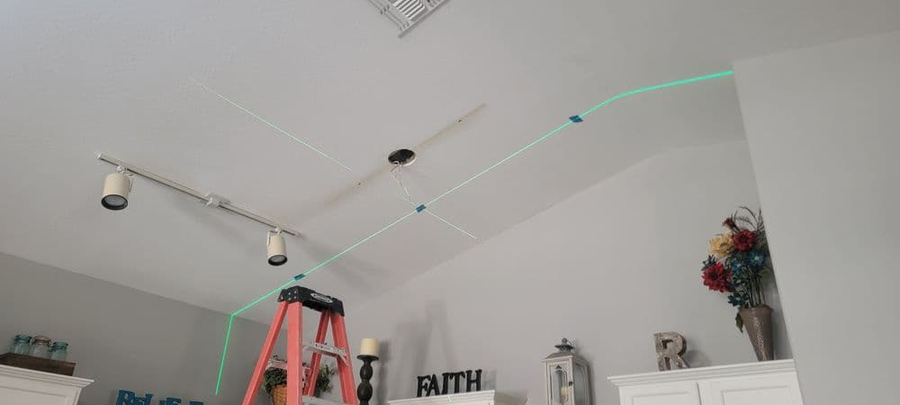 Laser level assisting with ceiling fan installation in a modern living room.