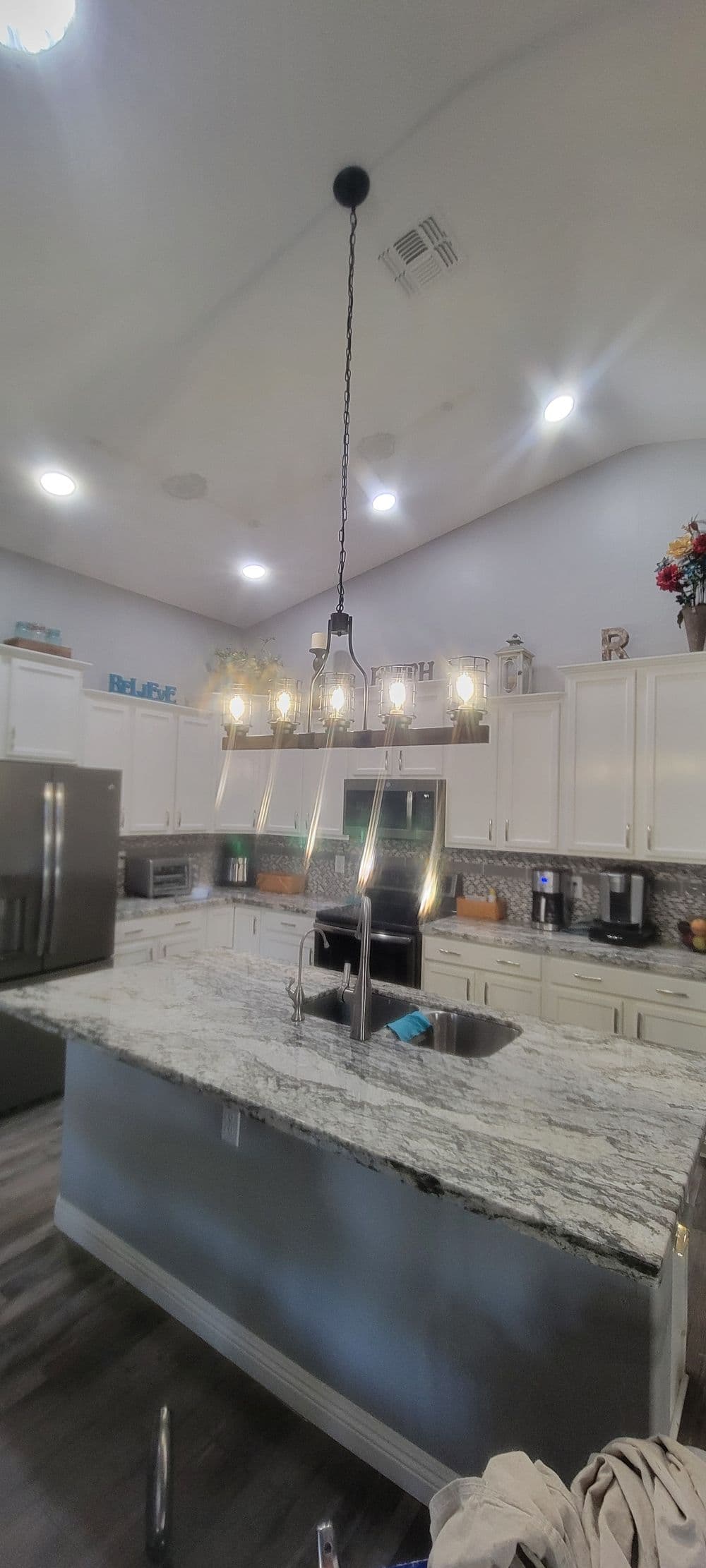 Modern kitchen with granite island, pendant lights, stainless steel appliances, and bright decor.