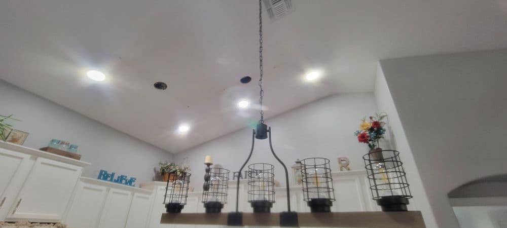 Chandelier with black wire cages and candles, illuminating a modern kitchen.